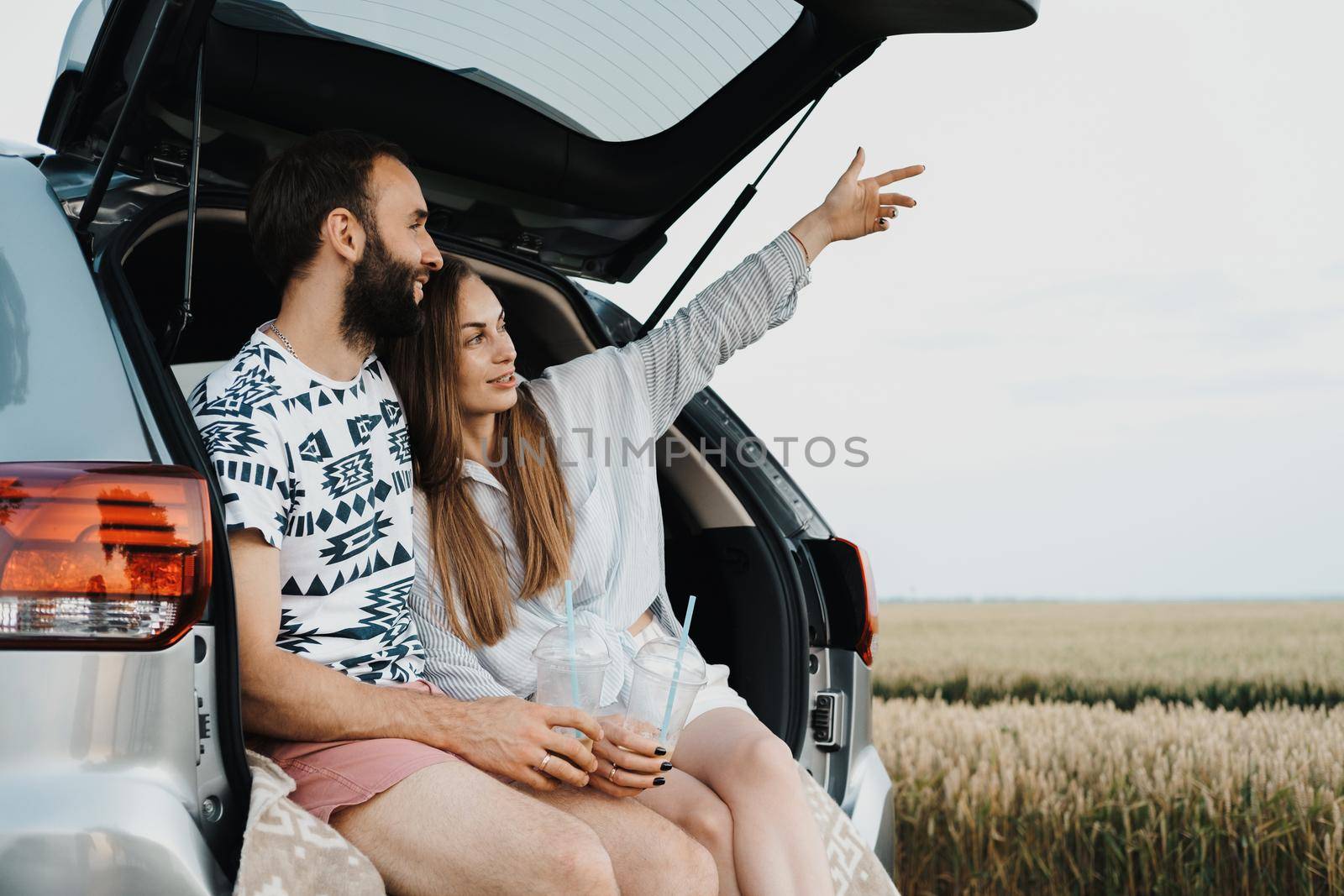 Middle-aged couple making stop while on a road trip, caucasian cheerful woman and man drinking coffee in trunk of car