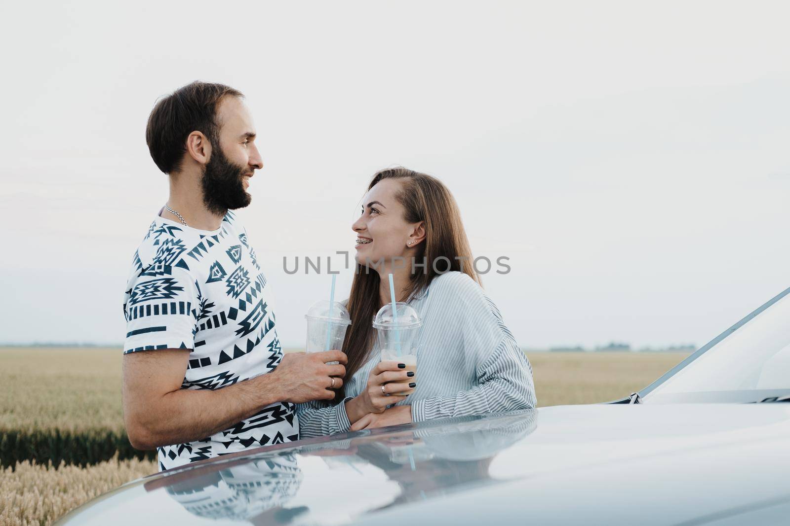 Caucasian cheerful woman and man drinking coffee outdoors near the car in the field, middle-aged couple making stop while on a road trip by Romvy