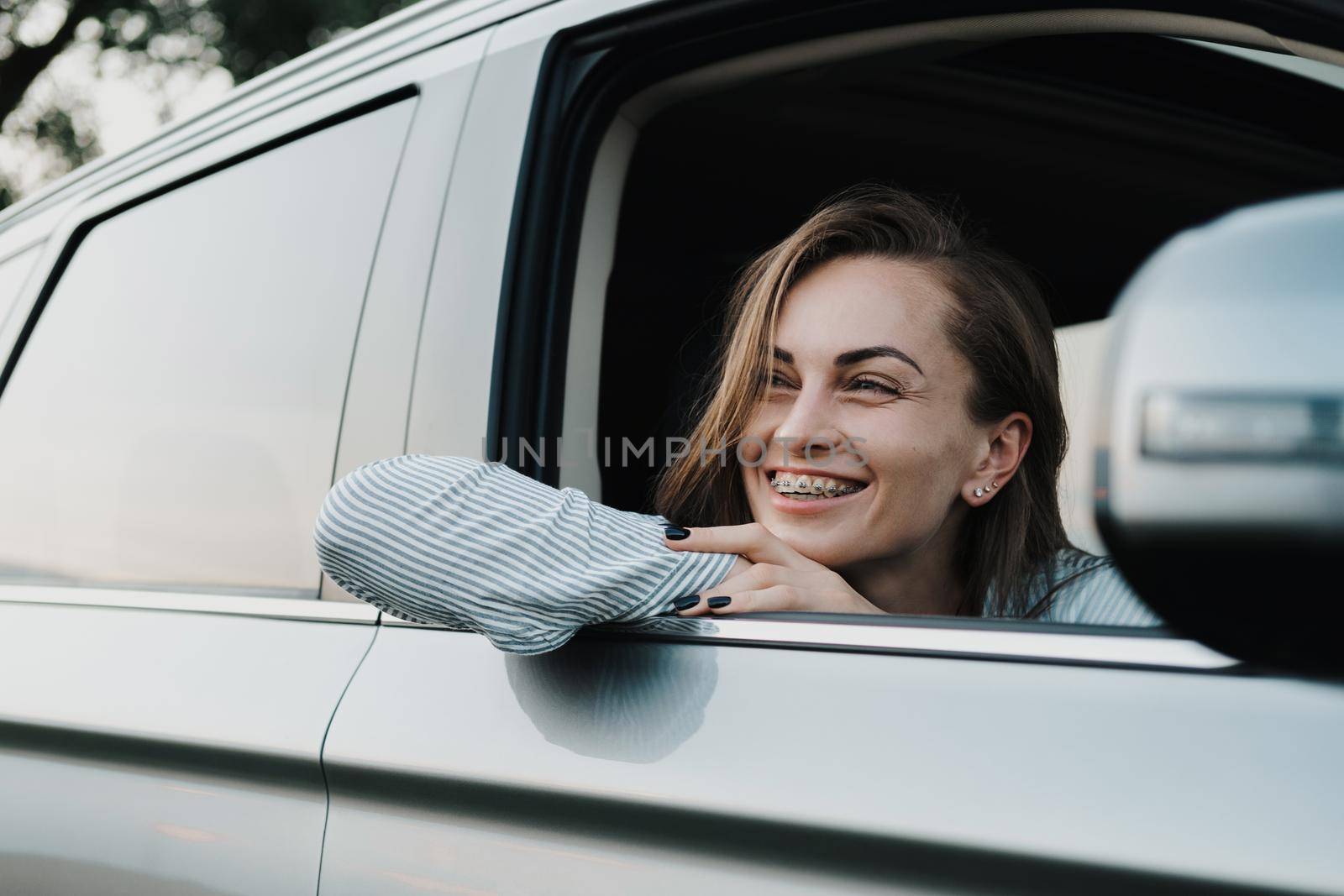 Cheeful caucasian woman with braces enjoying road trip and looking out from car window