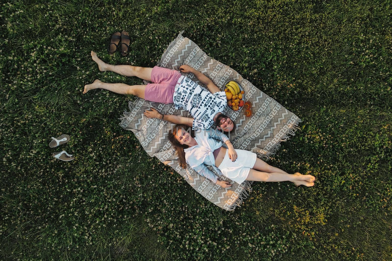 Aerial shot top-down view of middle-aged couple enjoying picnic in the field, caucasian man and woman lying on a blanket by Romvy
