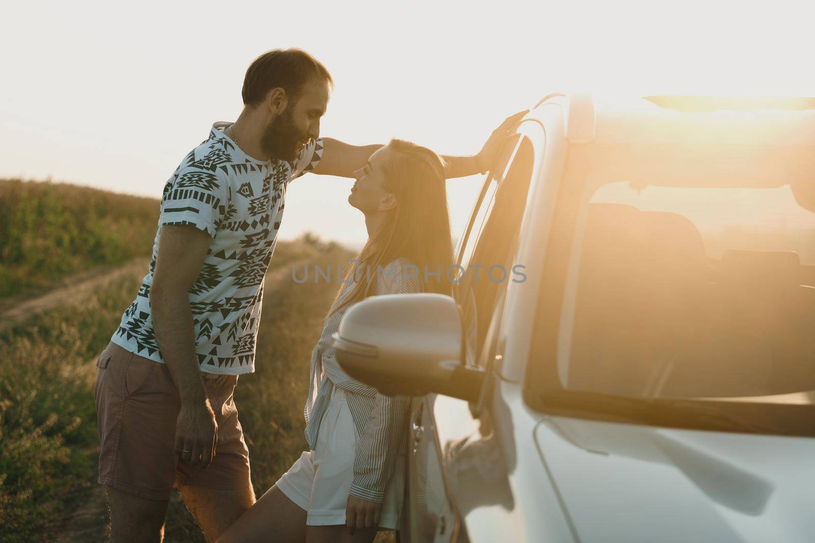 Man and woman standing near the car at sunset, middle-aged couple enjoying weekend outside the city by Romvy