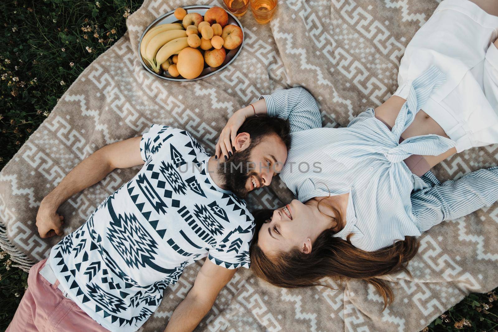 Top-down shot of cheerful man and caucasian woman laying on blanket and enjoying weekend picnic together, happy middle-aged couple having picnic outside the city by Romvy