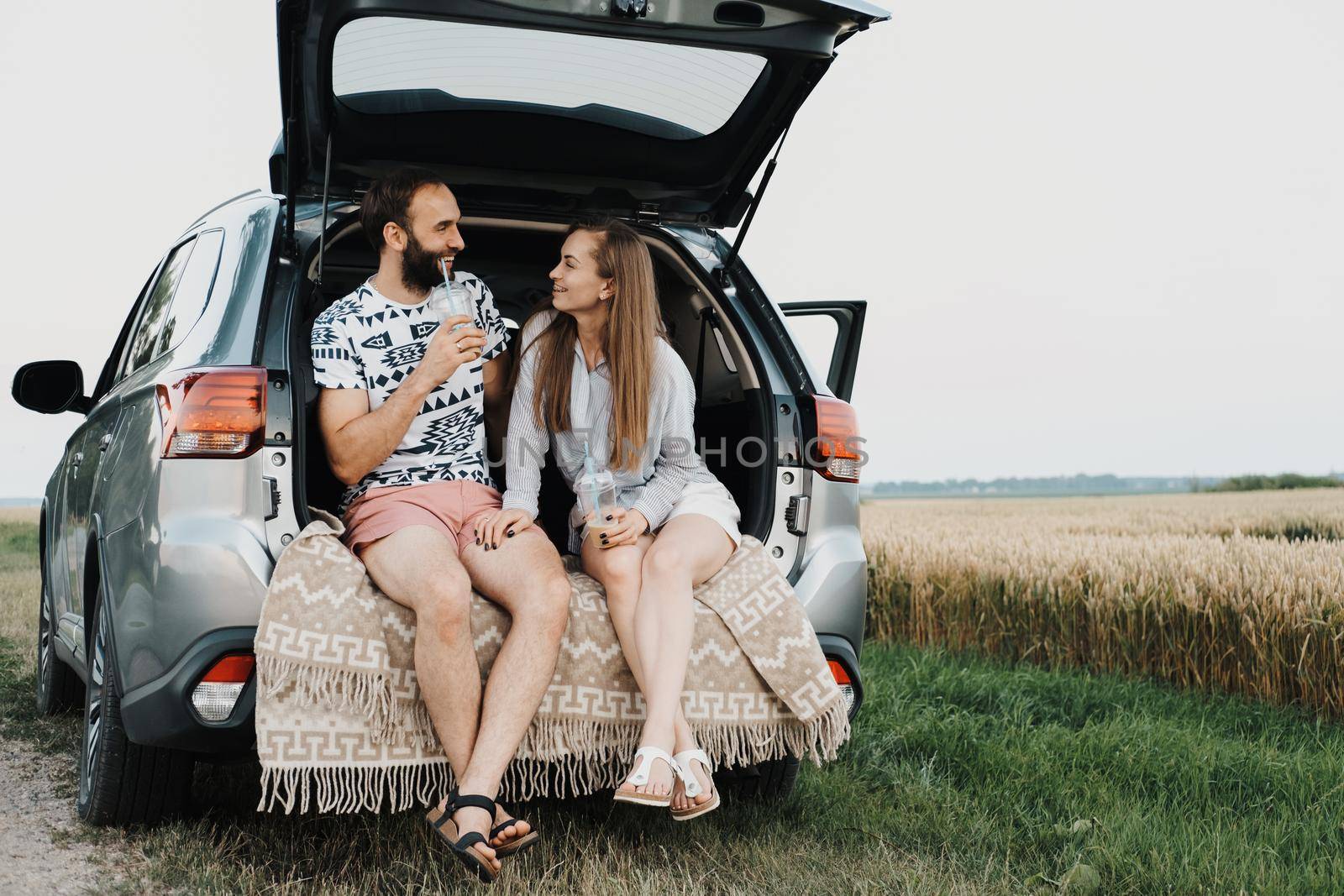 Caucasian cheerful woman and man drinking coffee in trunk of the car, middle-aged couple making stop while on road trip