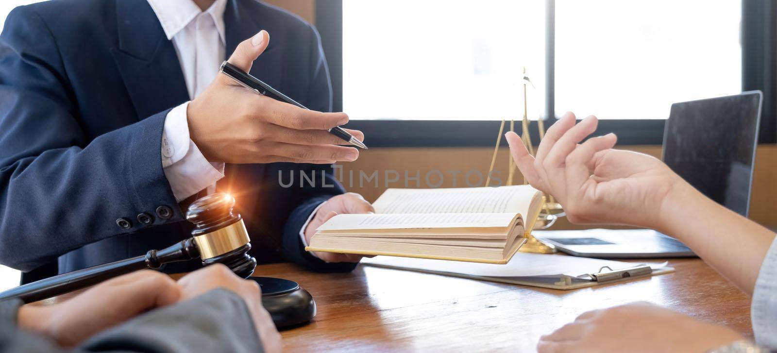 Lawyer hands holding a legal book and clarify the law to client while sign a contract at lawyer office.