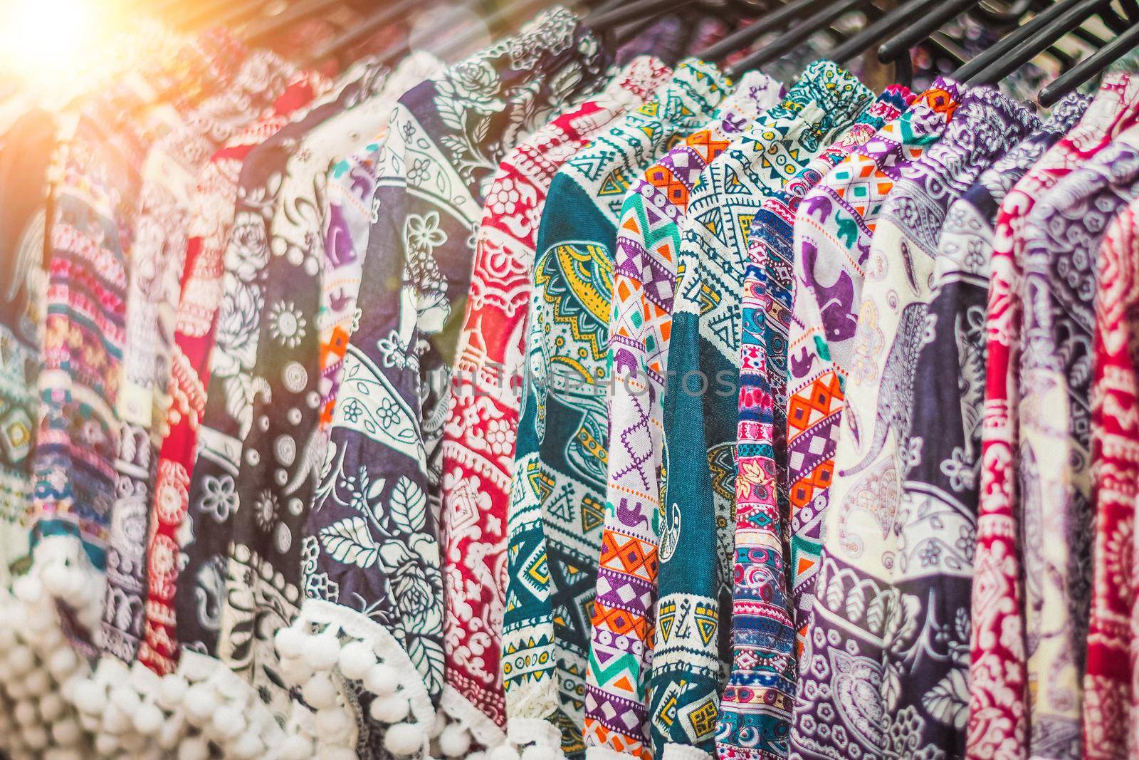 clothes hanging on a rack in a flea market Souvenir shop in Thailand by Petrichor