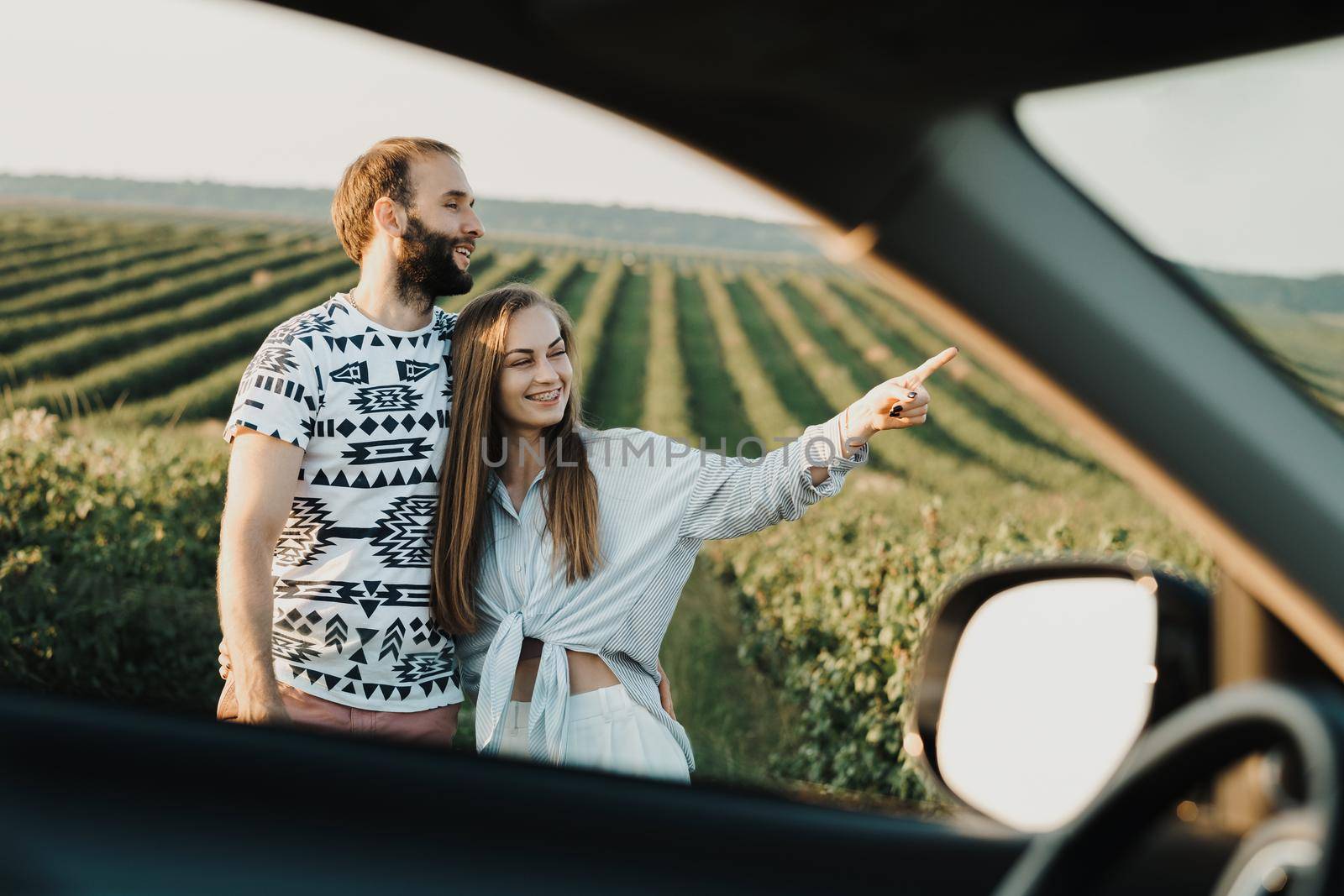 View through car window, happy middle-aged couple hugging together in beautiful fields, caucasian man and woman enjoying vacation outdoors