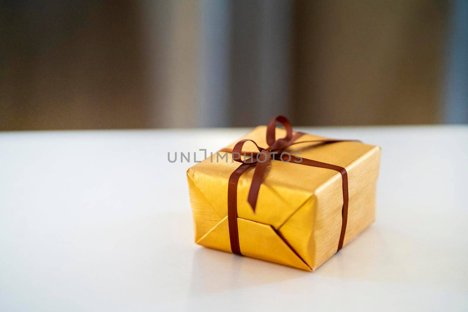 A cute little gift in a golden wrapper and with a ribbon lies on the table, a beautiful surprise for the holidays