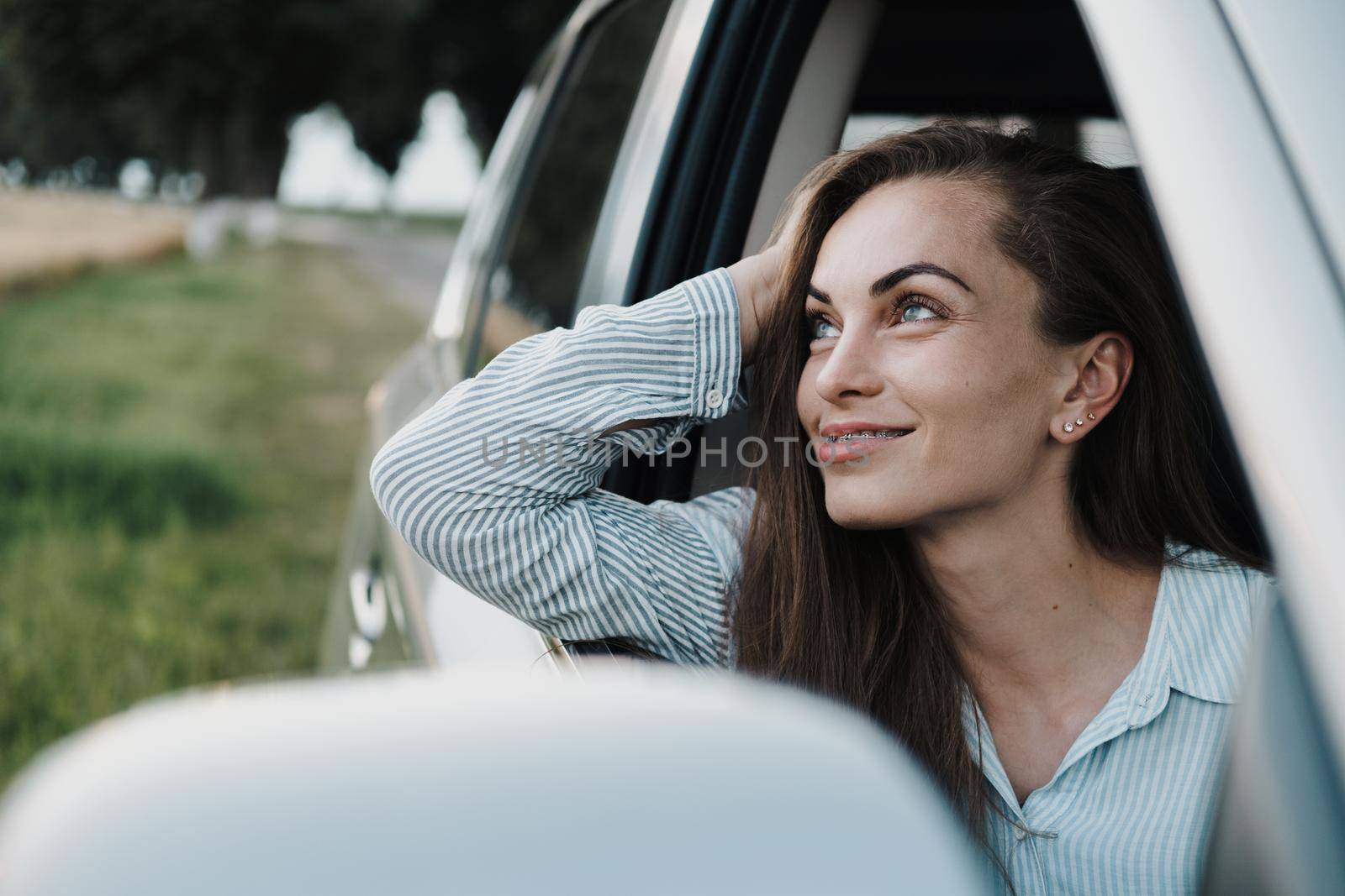 Cheeful caucasian woman with braces enjoying road trip and looking out from car window by Romvy