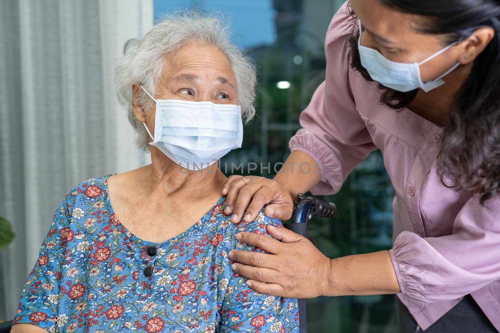 Caregiver help Asian senior or elderly old lady woman sitting on wheelchair and wearing a face mask for protect safety infection Covid 19 Coronavirus. by pamai