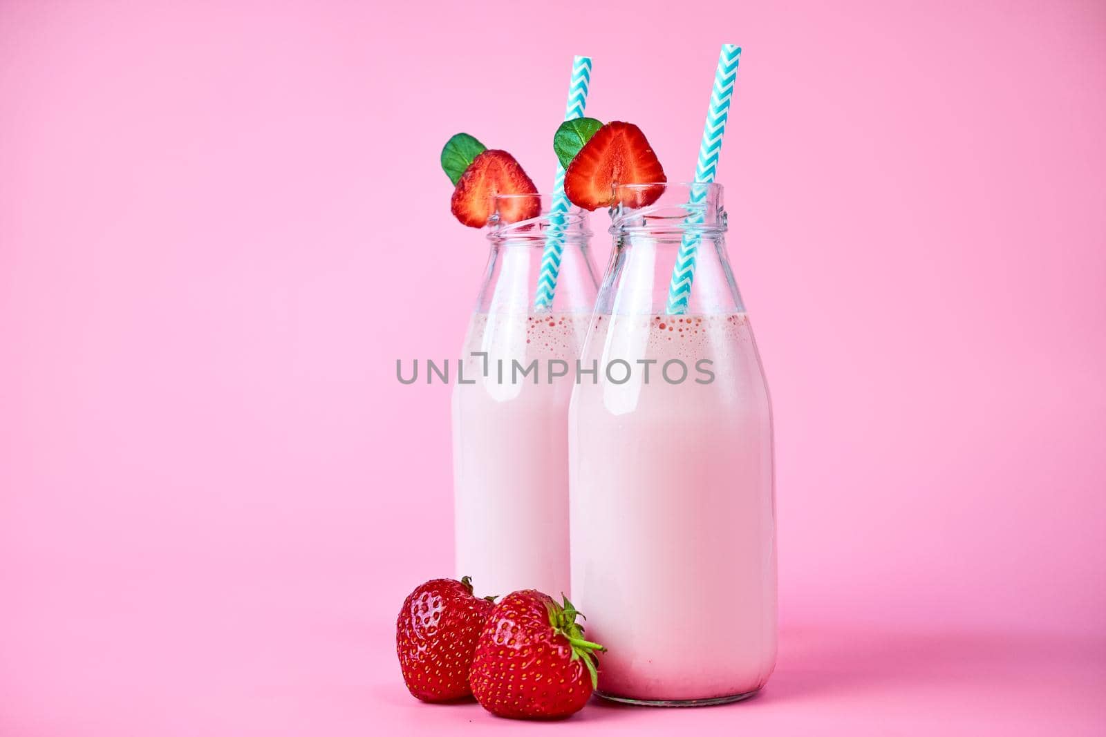 Close-up strawberry smoothie or milkshake in glass jar with berries on pink background. Healthy summer drink