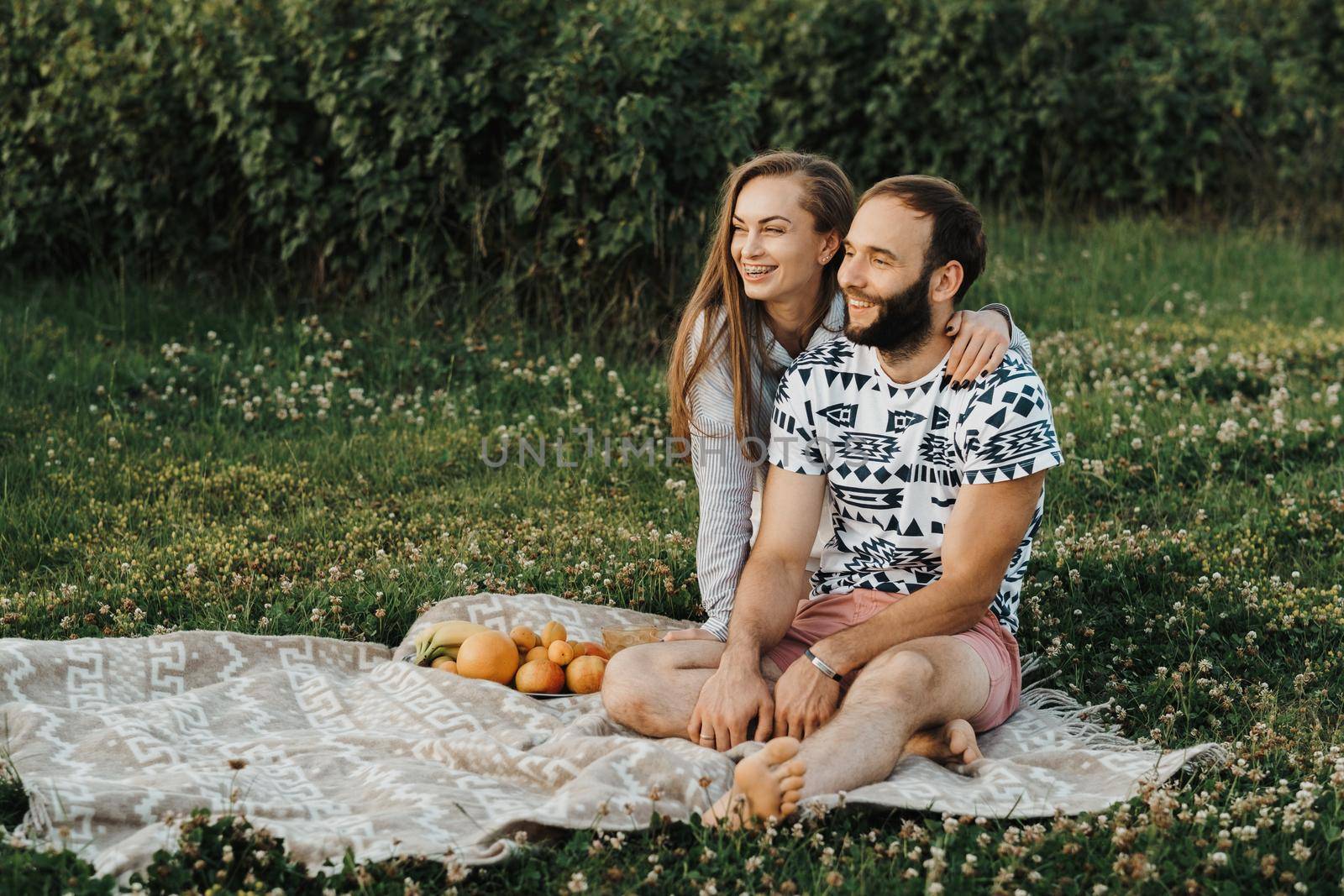 Cheerful man and caucasian woman sitting on blanket and enjoying weekend picnic together, happy middle-aged couple having picnic outside the city by Romvy