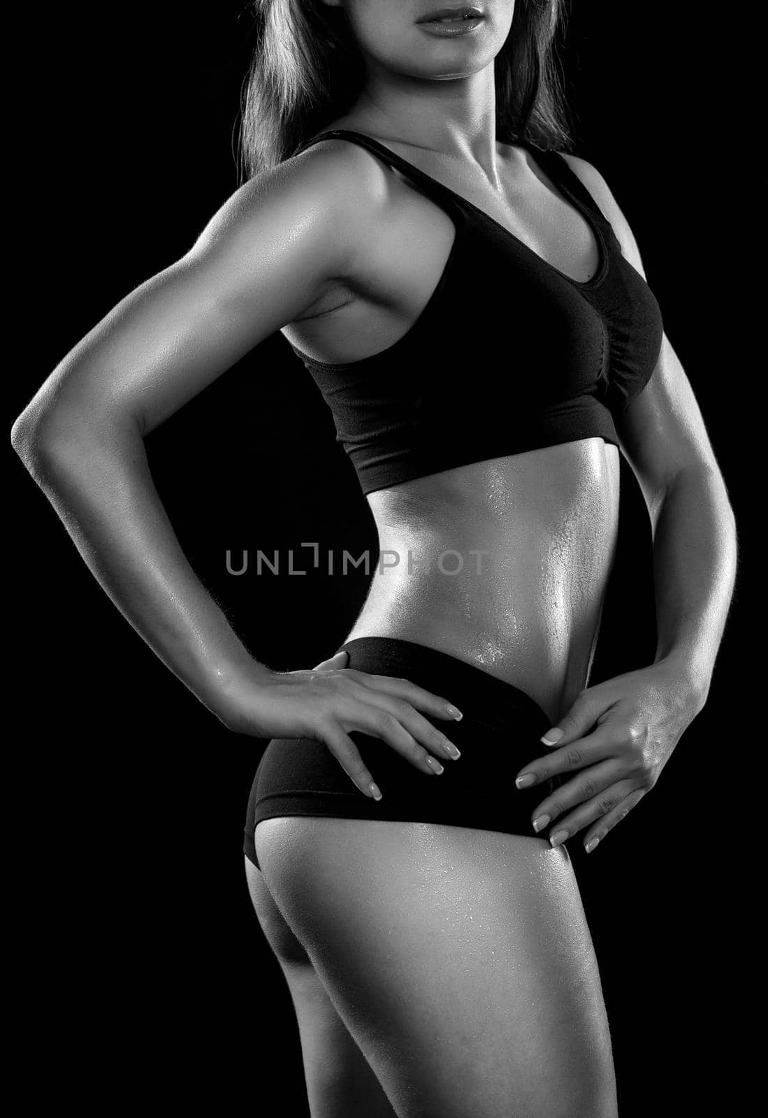 Young sporty girl with the sweat on the skin is poses for the camera against a black background. Black and white photography.