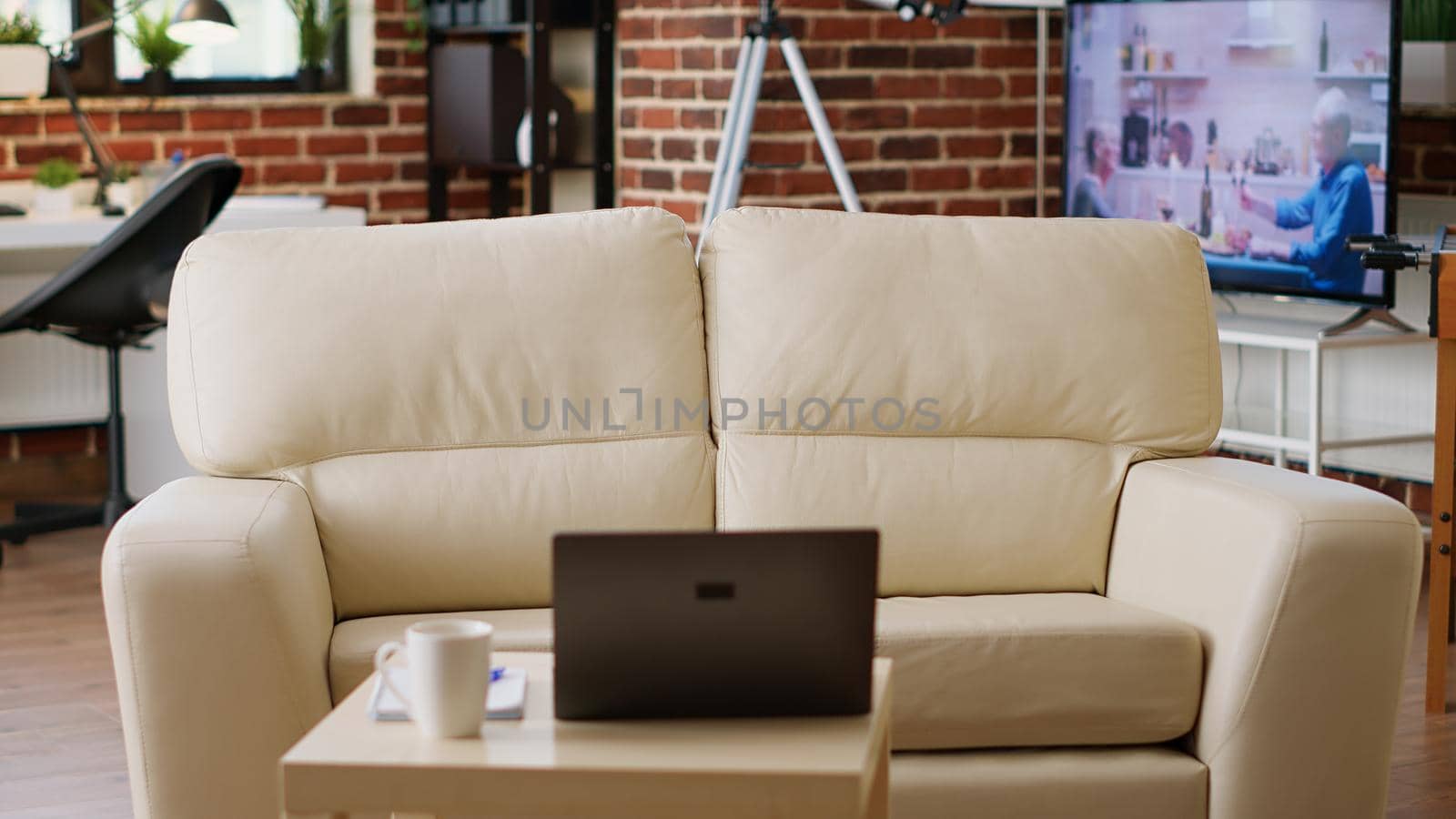 Empty brick wall house with nobody in it and with modern portable computer on desk. Interior of modern and cozy apartment living room with comfortable sofa and laptop on coffee table