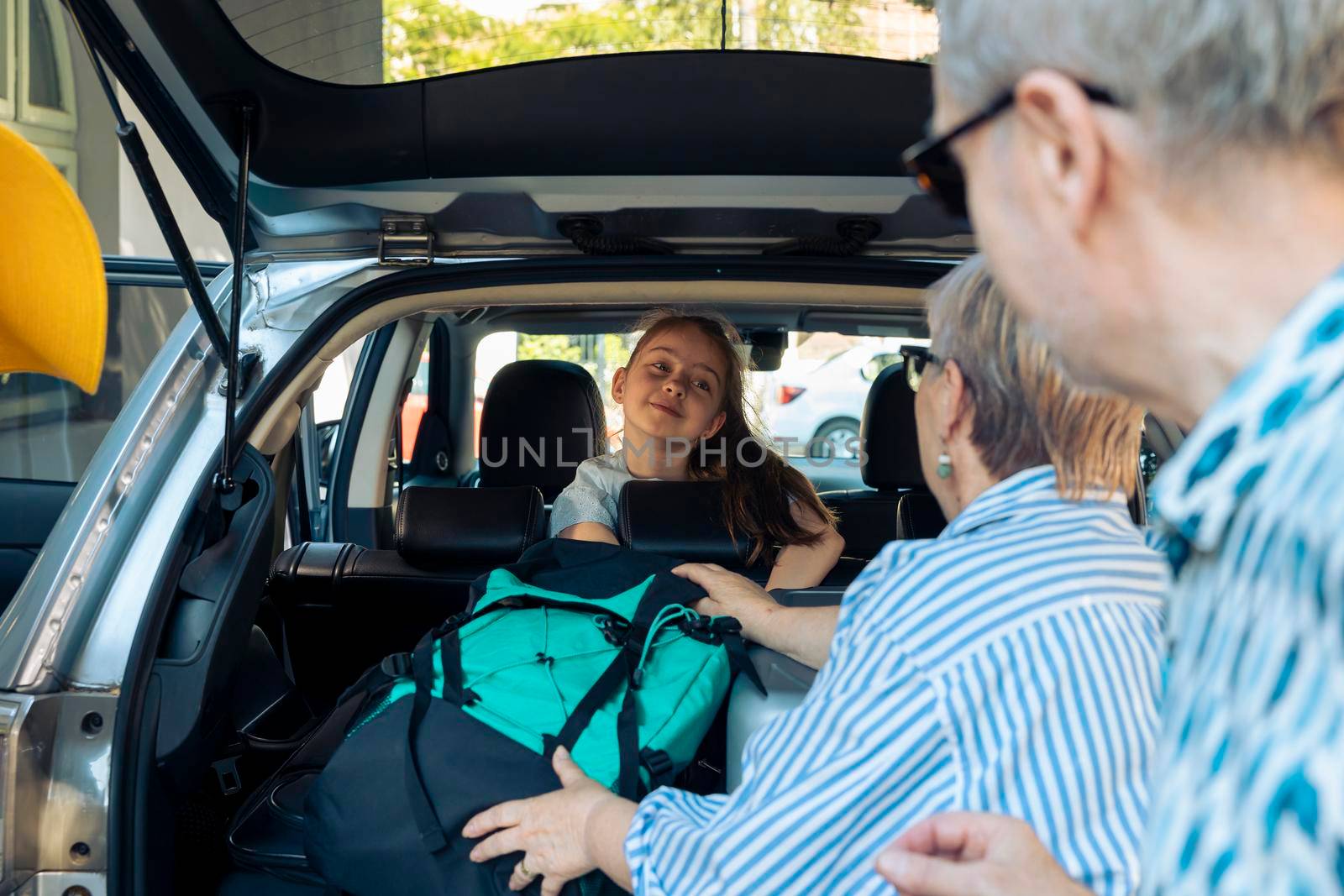Little girl going on vacation with family, preparing to leave on summer holiday at seaside with parents and grandparents. Putting luggage in vehicle trunk to travel to journey destination.