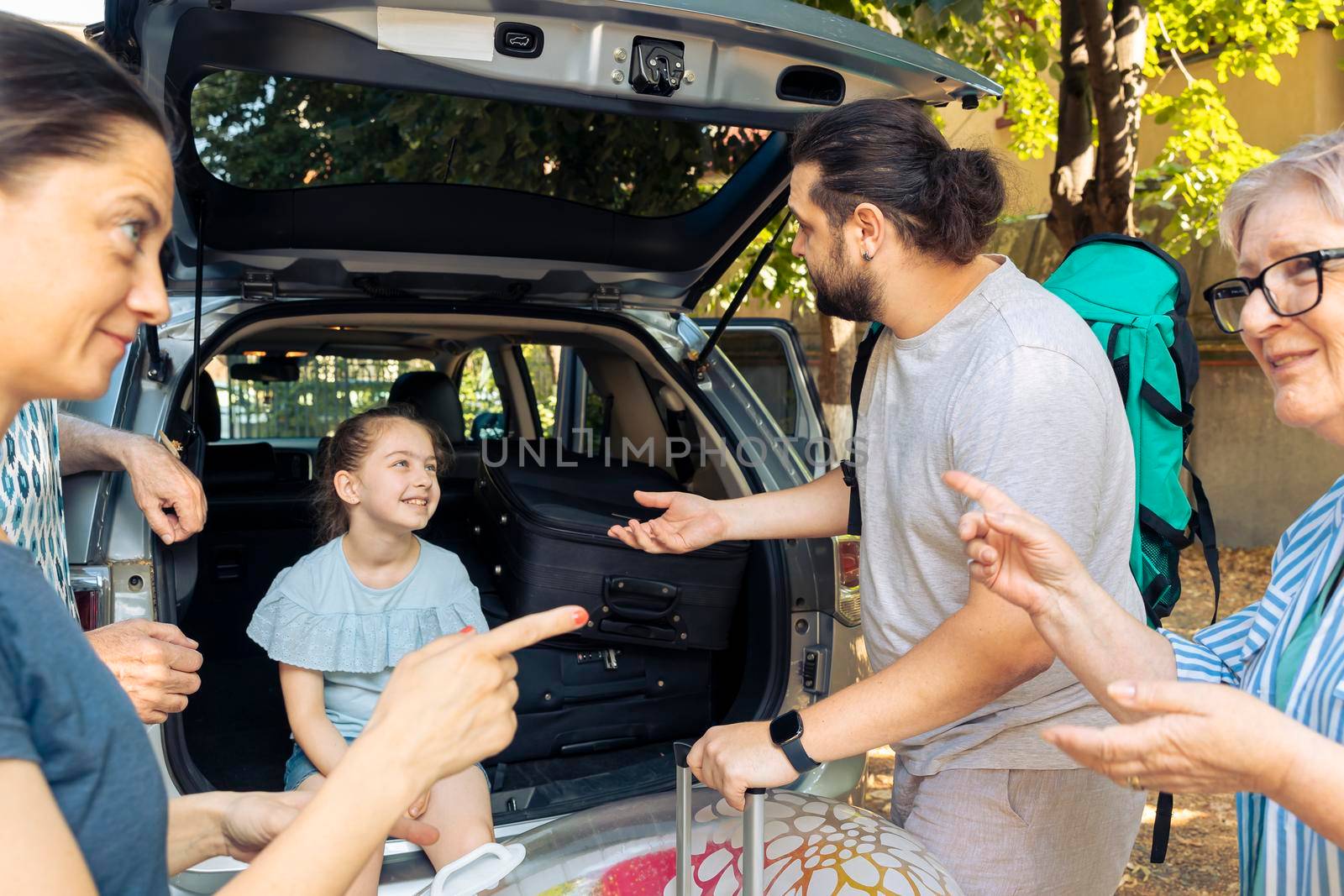 European family going on vacation journey, loading baggage and inflatable in car trunk to leave at seaside. Little kid, parents and grandparents travelling on summer holiday with vehicle.