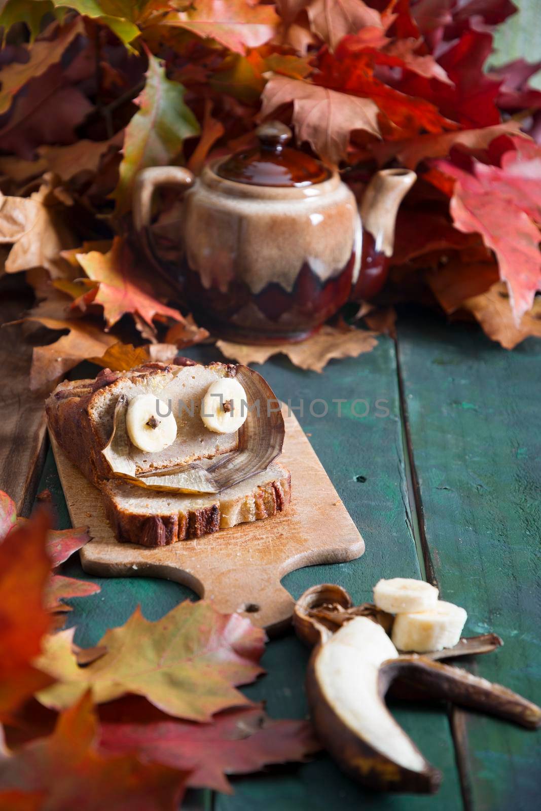 Creative still life of banana cake with eyes on a background of bright autumn leaves, copper coffee grinder and ceramic cup with coffee on a wooden background. High quality photo