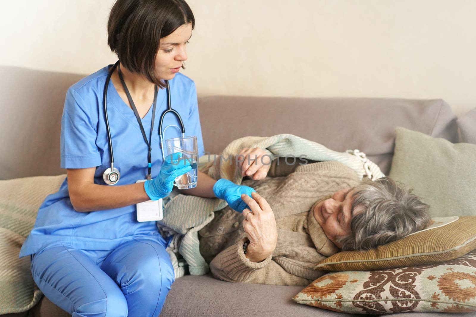 A young nurse is caring for an elderly 80-year-old woman at home, she asks about the well-being of a pensioner who lies and rests in bed. Happy retired woman and trust between doctor and patient.