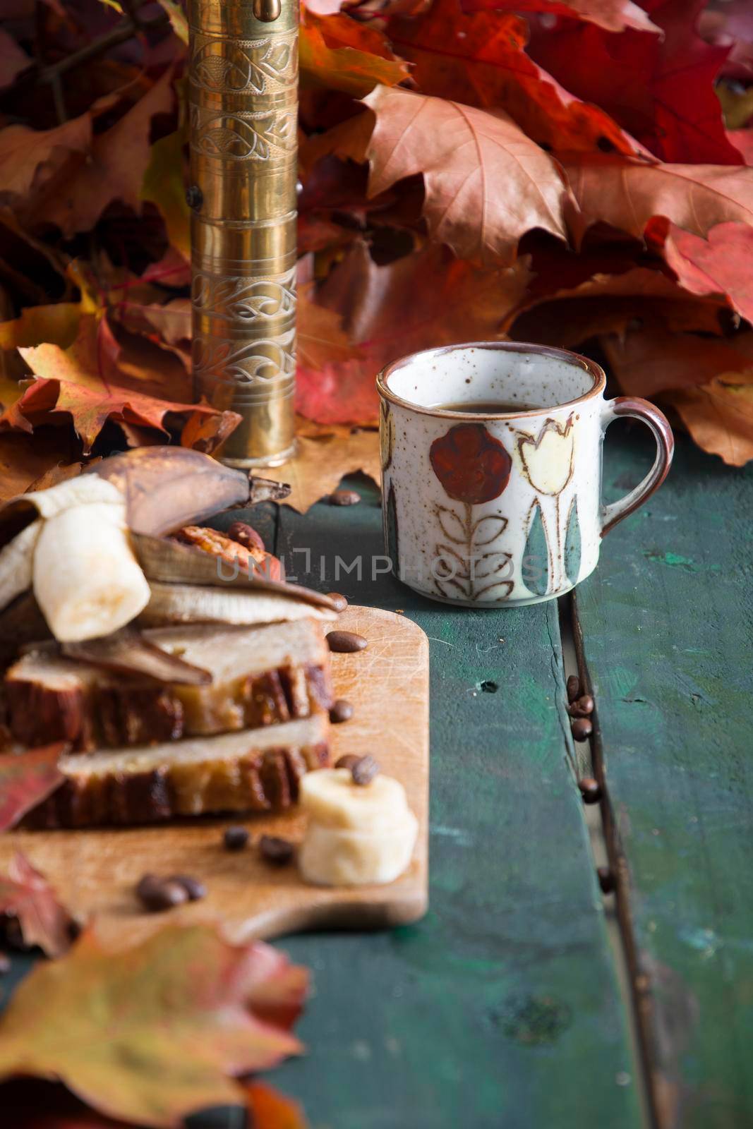 Banana pie on a background of autumn bright leaves, a copper coffee grinder and a ceramic cup with coffee on a wooden background. High quality photo