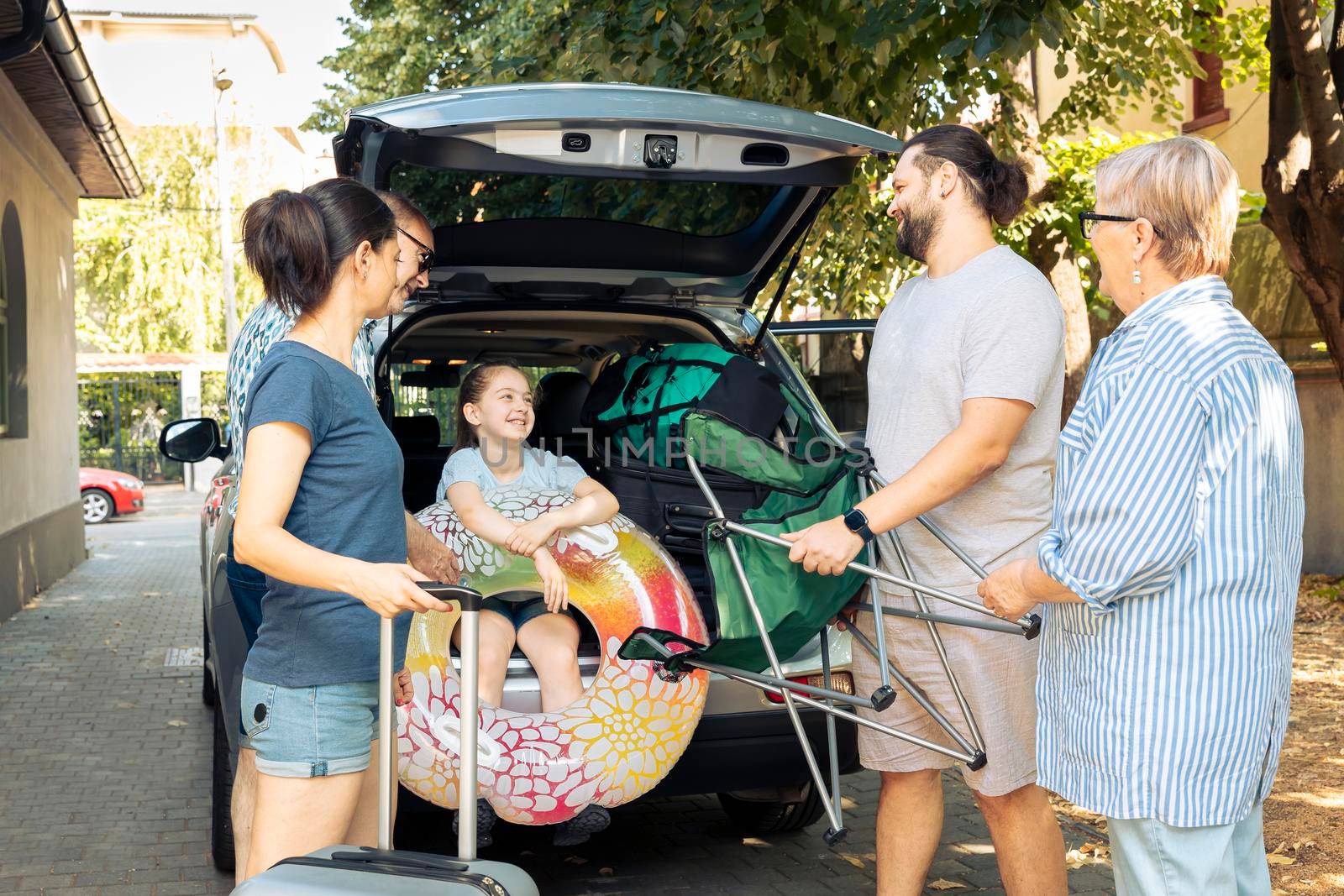 Happy people loading baggage in trunk to travel on seaside vacation holiday, big family preparing for adventure trip. Small child with parents and grandparents travelling with luggage during summer.