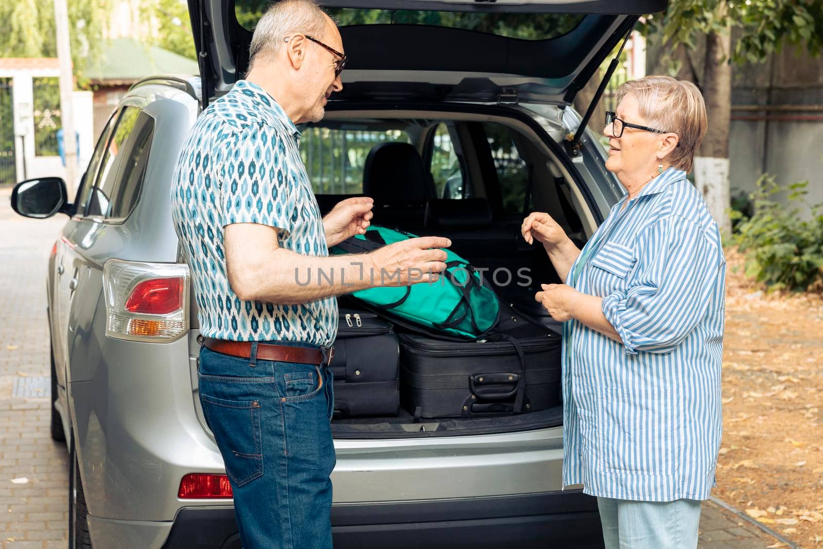 Senior couple travelling on vacation by car, talking about urban adventure after loading baggage and luggage in vehicle. Husband and wife preparing to leave on retirement holiday trip.