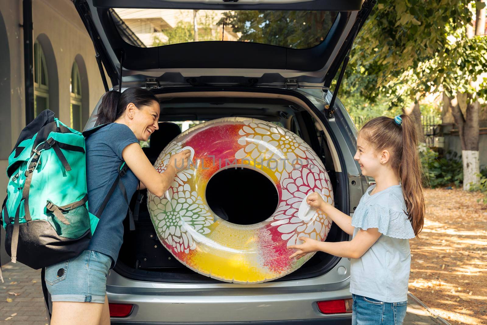 Mother and young child travelling by car, going to seaside with inflatable and luggage. Loading suitcase, baggage and travel bags in trunk of vehicle to leave on summer holiday vacation.