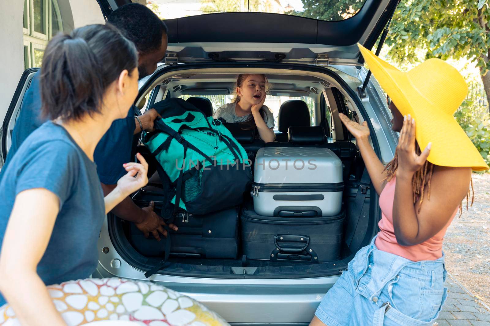 Little girl and diverse people going on vacation, loading travel bags in vehicle trunk. Leaving on holiday adventure with family and friends, putting suitcase or trolley in automobile before roadtrip.