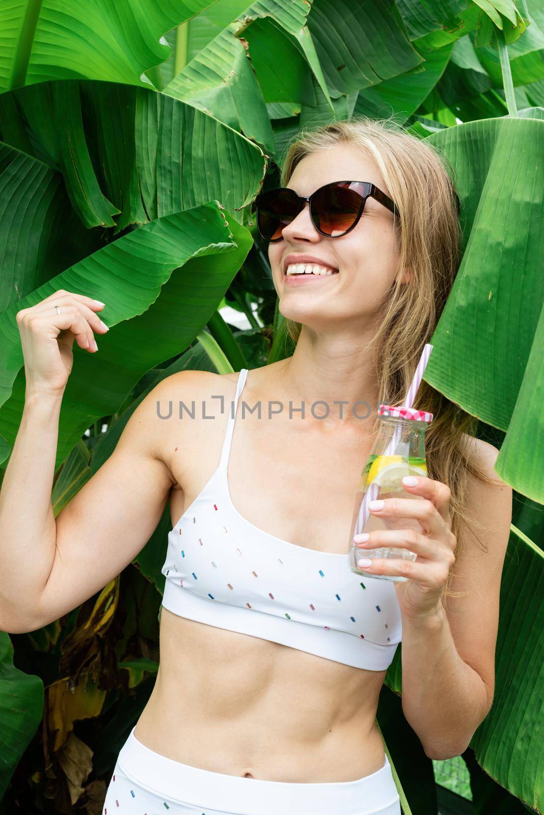 Summer vacation. Beautiful woman in white swimsuit with long hair and palm leaves. Beautiful caucasian girl in stylish swimwear in tropical nature