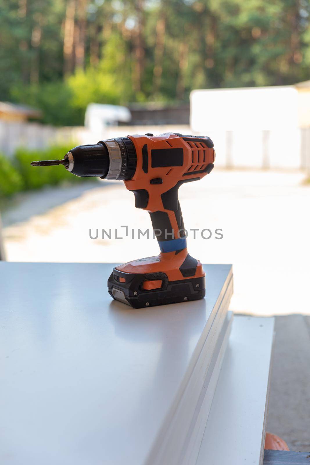 Cordless screwdriver stands on a wooden panel. A wireless tool for working outdoors in the absence of an electrical network.