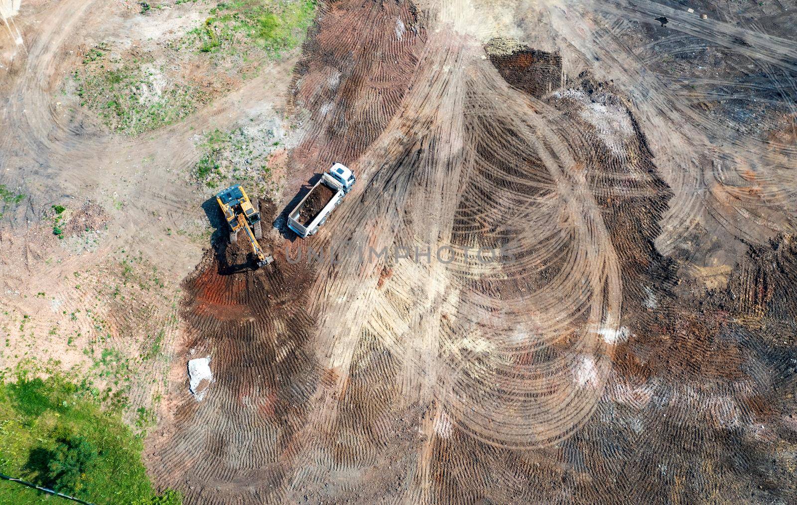 Aerial top view of excavator and dump trucks working at the construction site