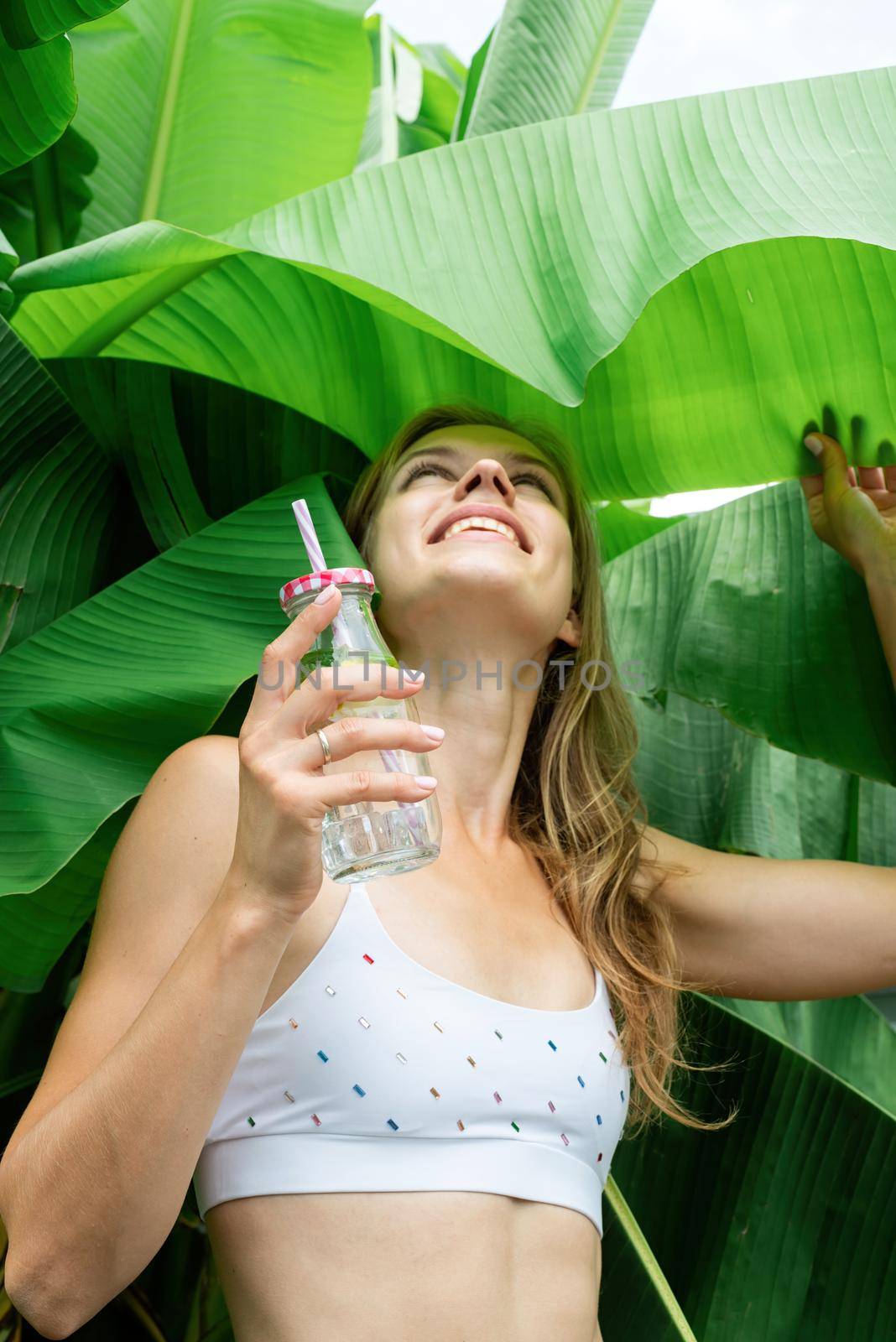 Summer vacation. Beautiful woman in white swimsuit with long hair and palm leaves. Beautiful caucasian girl in stylish swimwear in tropical nature