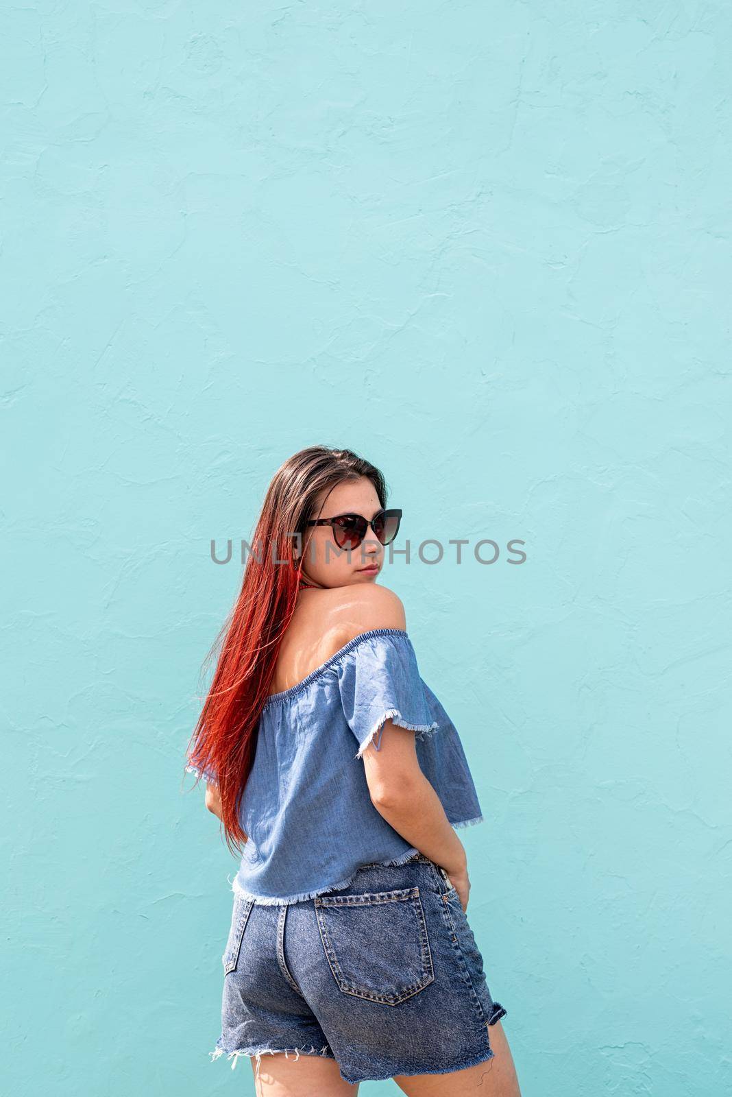 Attractive young woman in summer clothes and sunglasses, dancing on blue wall background at street