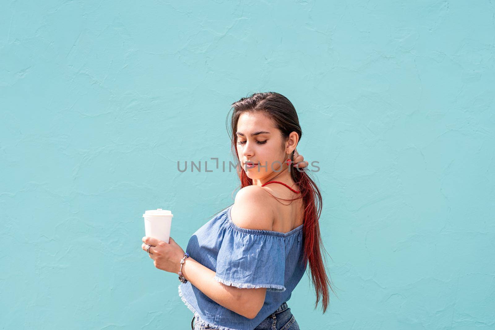 cheerful trendy woman with red hair drinking coffee dancing on blue wall background at street by Desperada