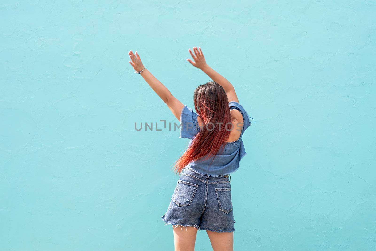Attractive young woman in summer clothes and sunglasses, dancing on blue wall background at street