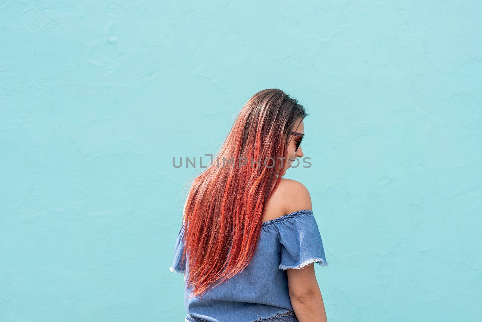 Attractive young woman in summer clothes and sunglasses, dancing on blue wall background at street