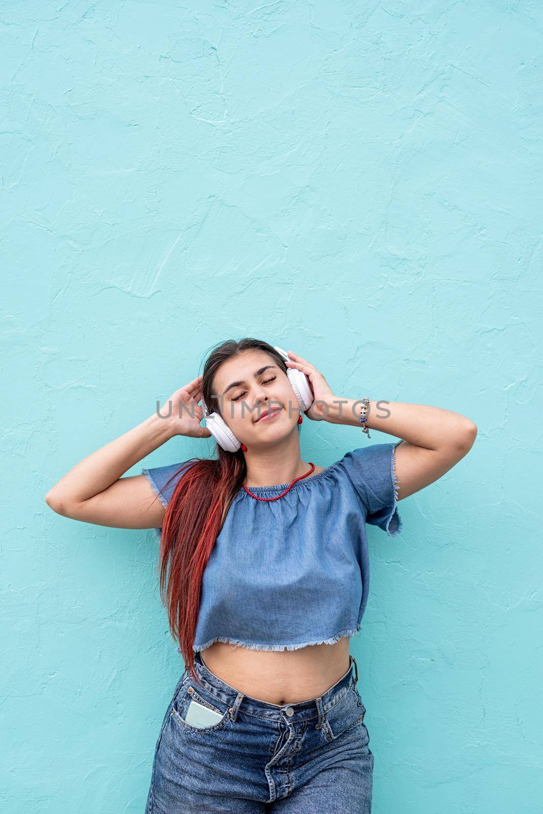 Attractive young woman in summer clothes and sunglasses listening to the music on blue wall background at street