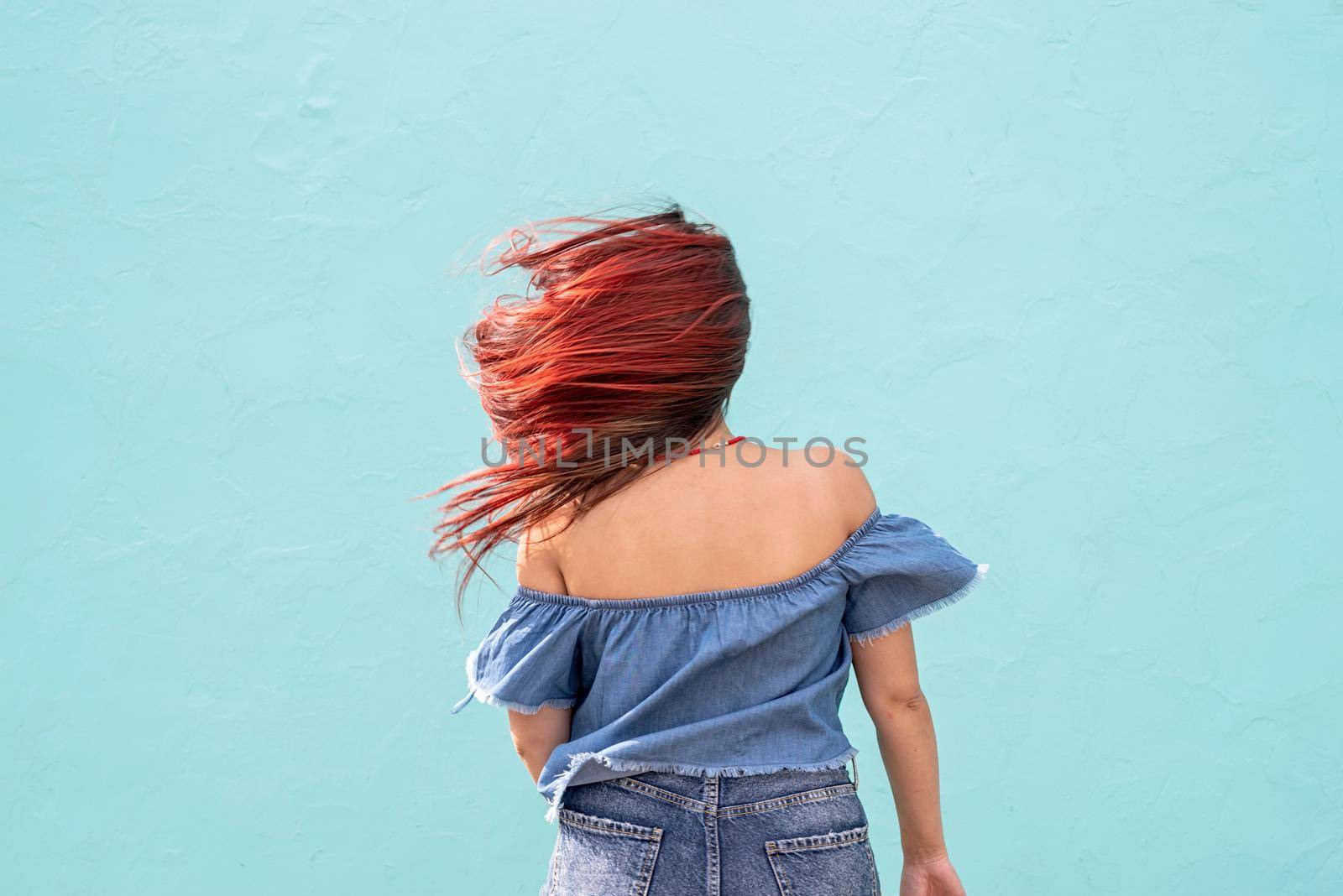 cheerful trendy woman with red hair dancing on blue wall background at street by Desperada