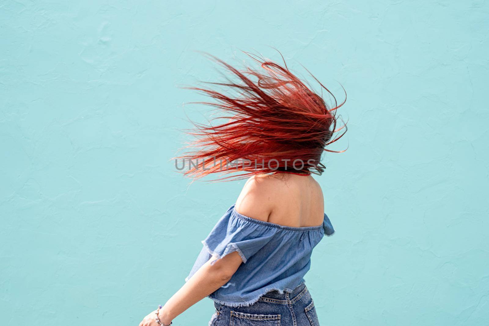 cheerful trendy woman with red hair dancing on blue wall background at street by Desperada