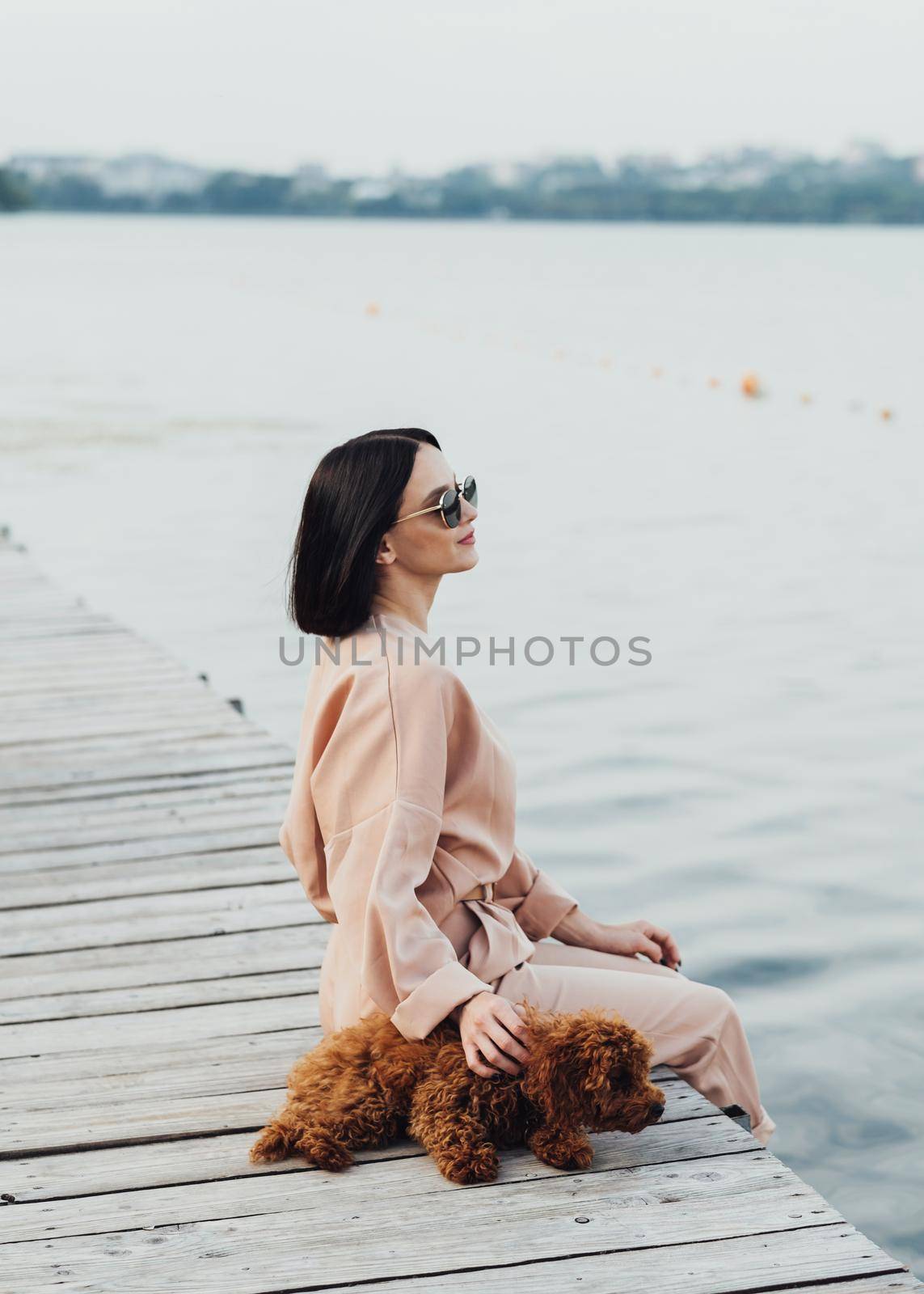 Brunette woman sitting on the pier with her redhead dog toy poodle