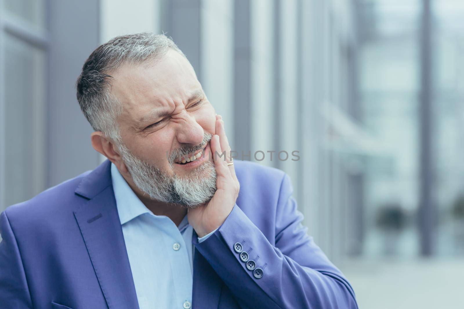 Close-up photo portrait of senior gray-haired businessman, experienced businessman outside office building, having severe toothache