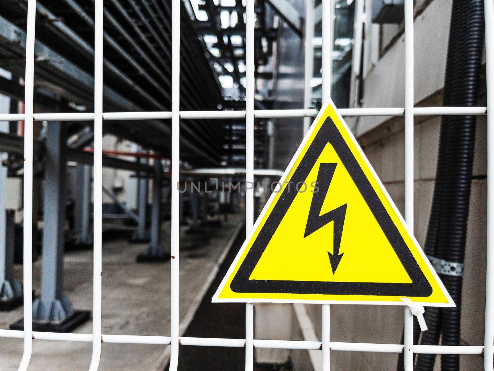 Danger Sign High voltage in the yellow triangle on the metal fence of the grid