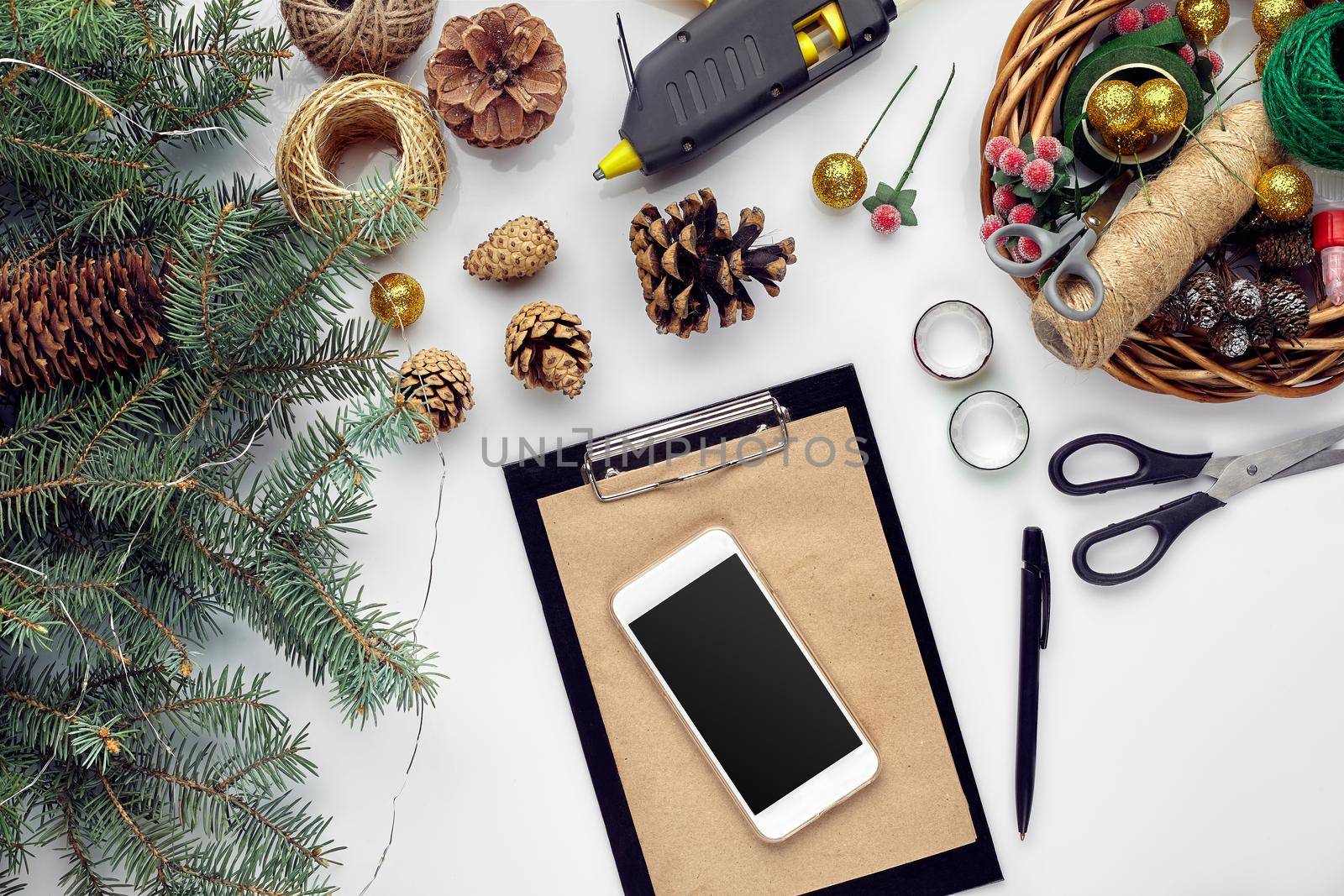 Preparing for Christmas or New Year holiday. Flat-lay of fur tree branches, wreaths, rope, scissors, craft paper over white table background, top view, copy space, horizontal composition
