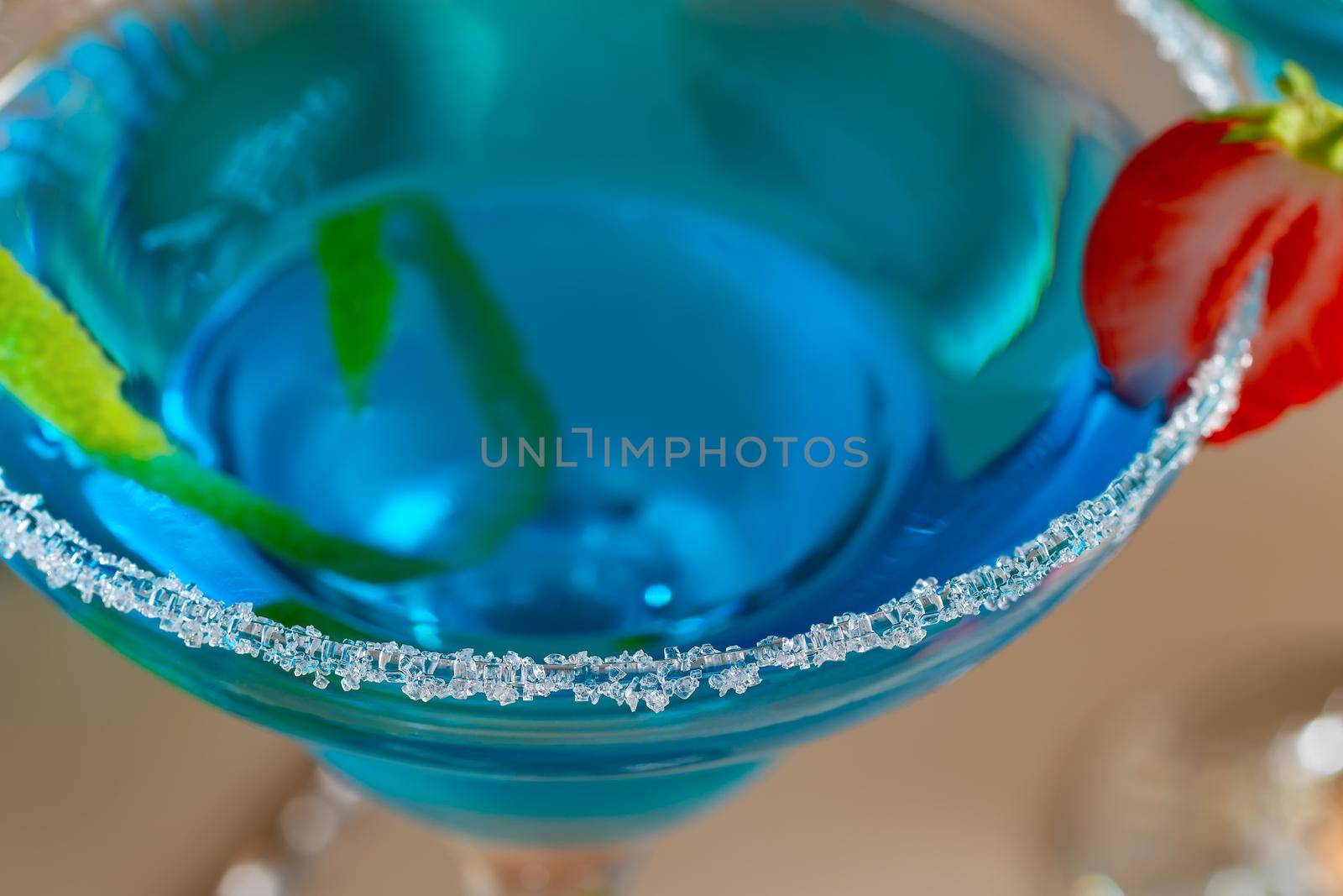 Glass with blue margarita cocktail garnished with lime zest and strawberries, selective focus by galsand