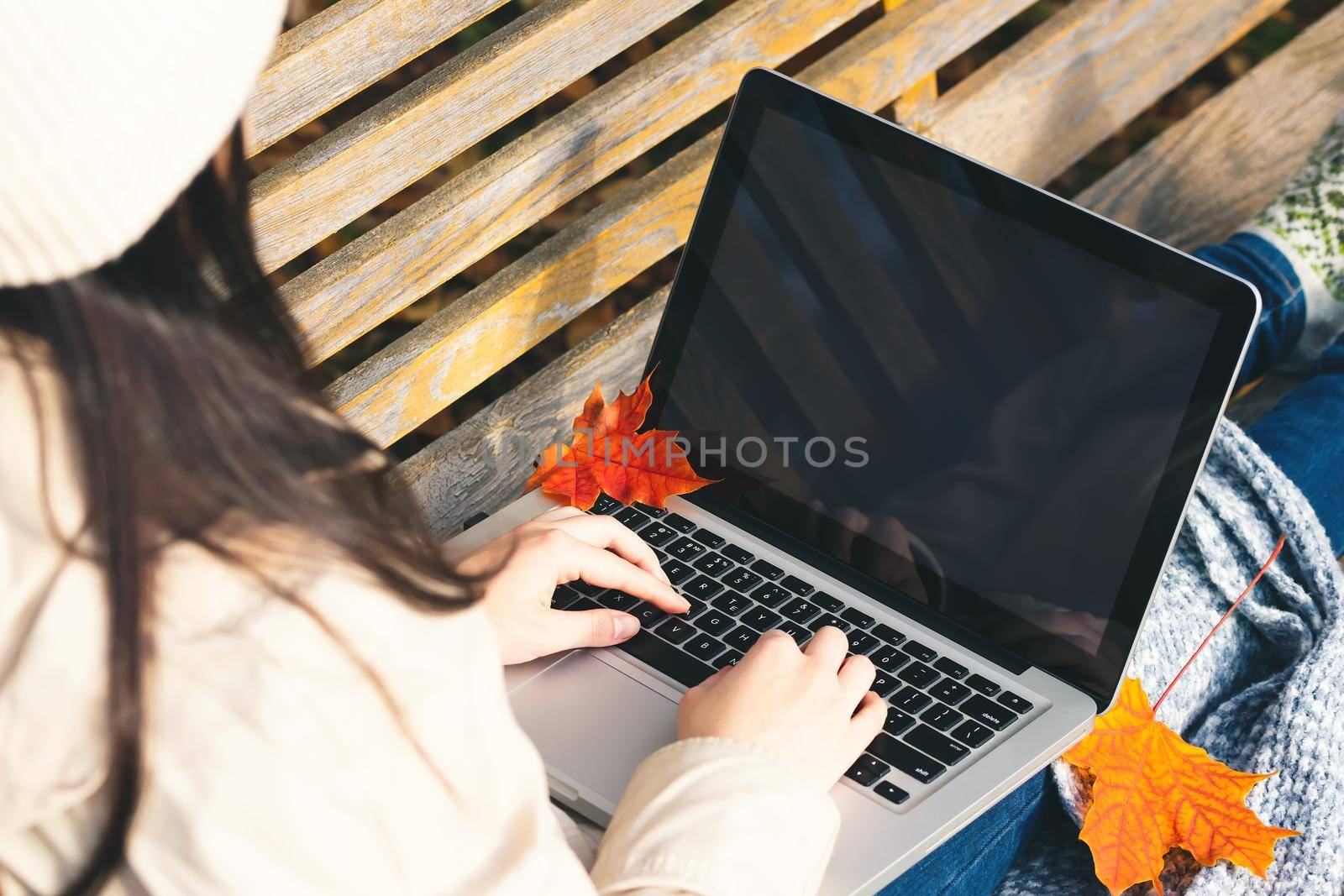 Girl uses a laptop while sitting on a bench in the autumn park. Blank for design on laptop screen by galsand