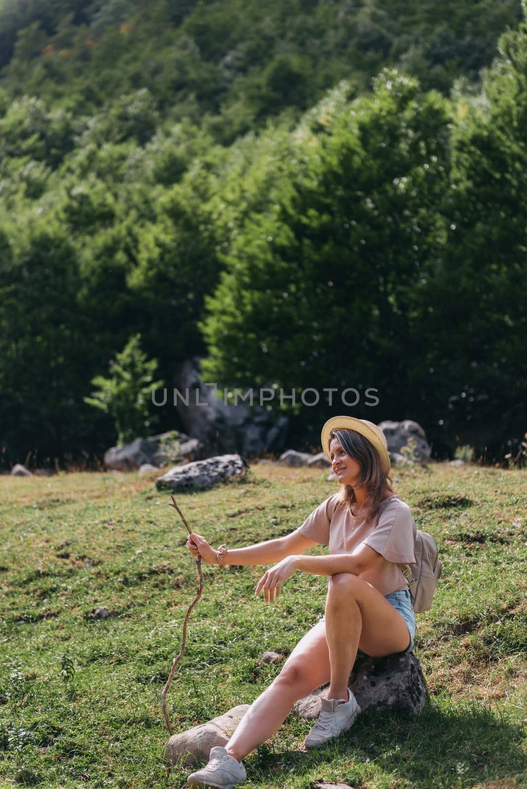 Travel, Lifestyle Concept. Beautiful woman enjoys views of the alpine village in the Alps mountains. Young woman sitting and relaxing on alpine mountain looking the cow eating a grass in the summer. Happy tourist girl traveling to Europe.