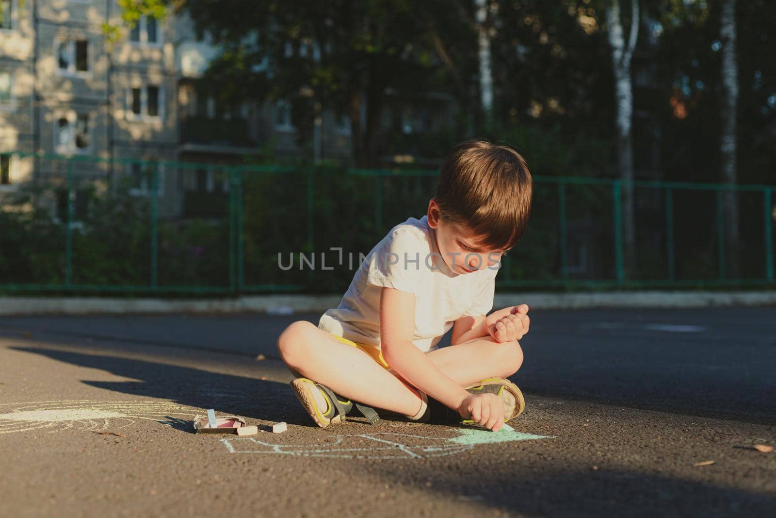 A boy draws a lifestyle with crayons on the asphalt . Children's classes. Children's drawings. Child psychology. Advertising of children's products