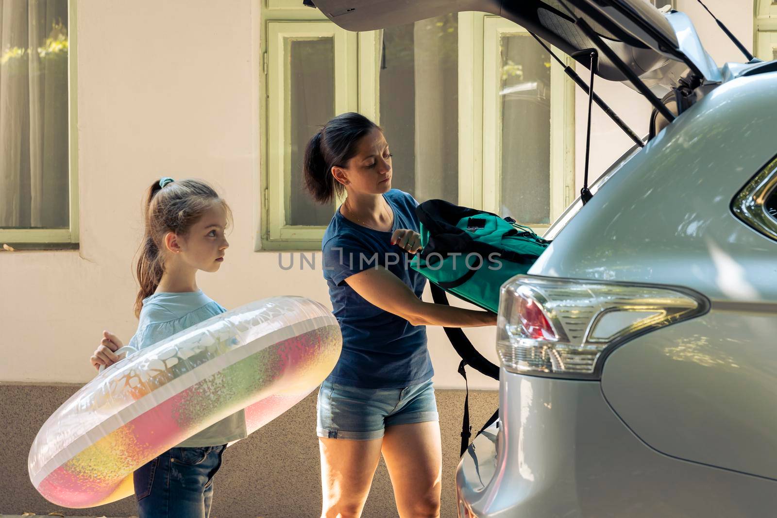 Mother with kid loading baggage in trunk, preparing to leave on road trip journey. Woman and small child travelling on holiday vacation at seaside during summer, happy recreation.