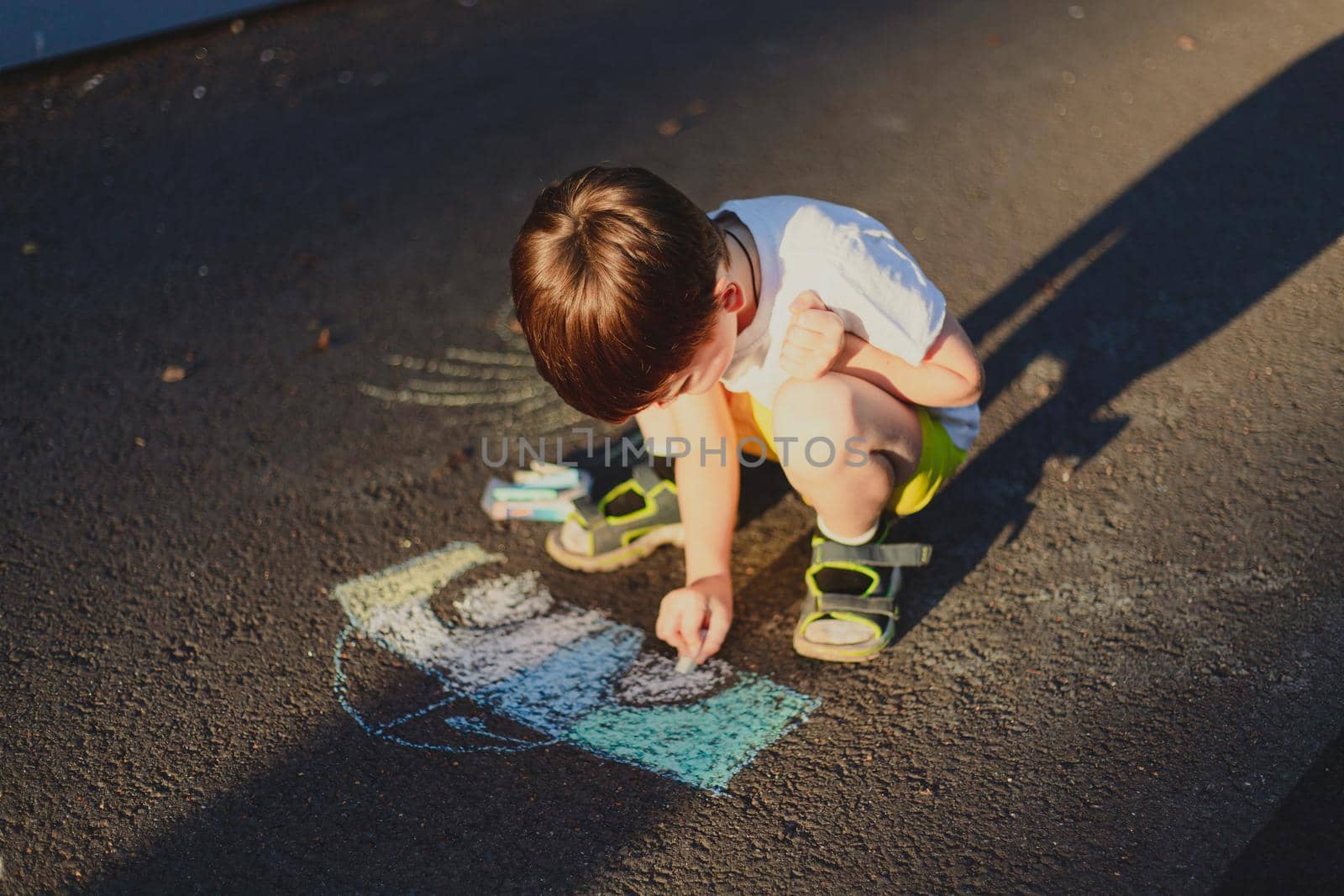 A boy draws a lifestyle with crayons on the asphalt . Children's classes. Children's drawings. Child psychology. Advertising of children's products