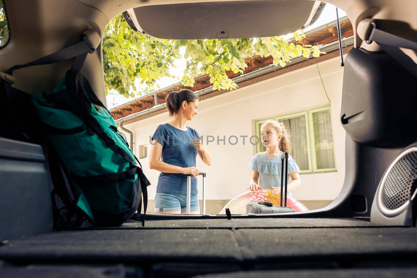 Mother with child loading trolley in trunk, getting ready to leave on seaside vacation with travel bags and inflatable. Small family putting baggage in vehicle, travelling on summer holiday trip.