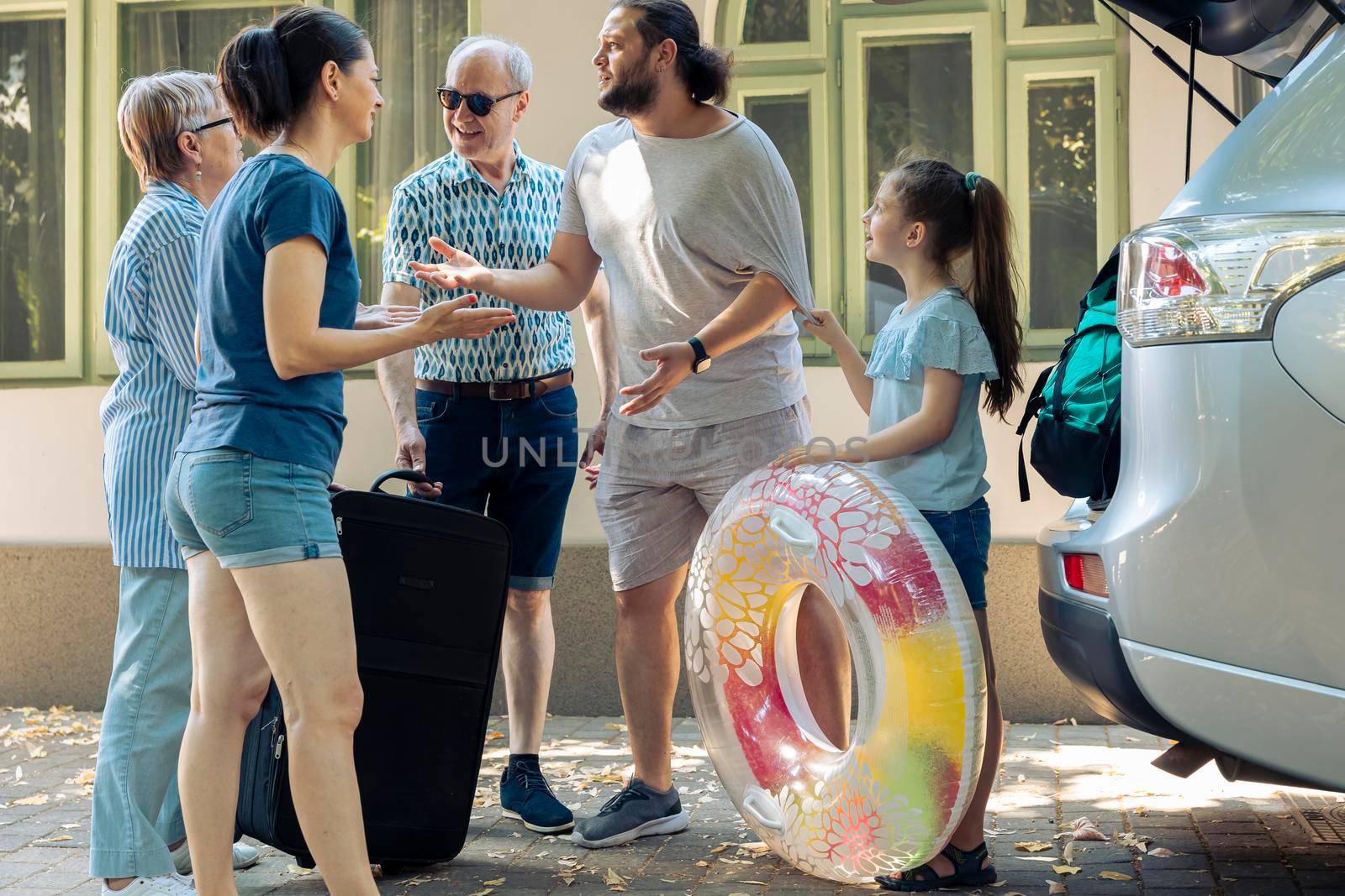 Young kid and family loading travel bags in trunk of car, preparing to leave on summer holiday. Travelling on vacation trip with automobile, parents and grandparents leaving on journey.