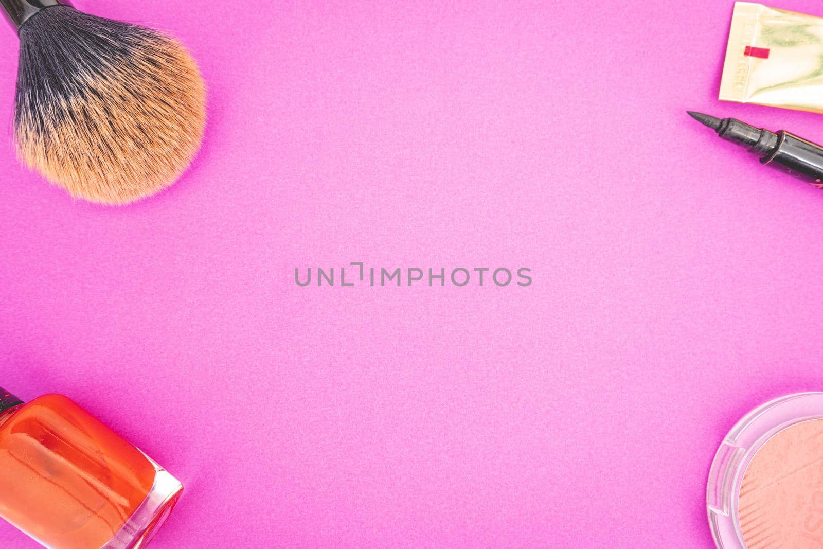 Flatlay of make up and beauty products on a pink background.